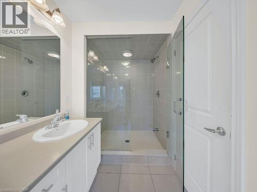Bathroom featuring a glass-enclosed shower with tile surround, a single vanity with a neutral countertop, white cabinetry with silver-tone hardware, and a large wall mirror - 76 Grassbourne Avenue, Kitchener, ON 