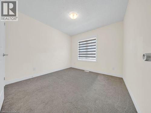 Neutral tone wall paint, grey carpet flooring, white baseboards, a window with horizontal blinds, and a flush mount ceiling light fixture - 76 Grassbourne Avenue, Kitchener, ON 