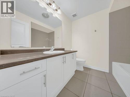 Bathroom featuring a spacious vanity with a dark countertop, white cabinetry with silver-toned hardware, an integrated sink with a chrome faucet, a large wall-mounted mirror, and tile flooring - 76 Grassbourne Avenue, Kitchener, ON 