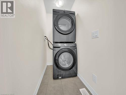 Dedicated laundry area featuring a stacked washer and dryer unit, neutral wall paint, white trim, and tiled flooring - 76 Grassbourne Avenue, Kitchener, ON 