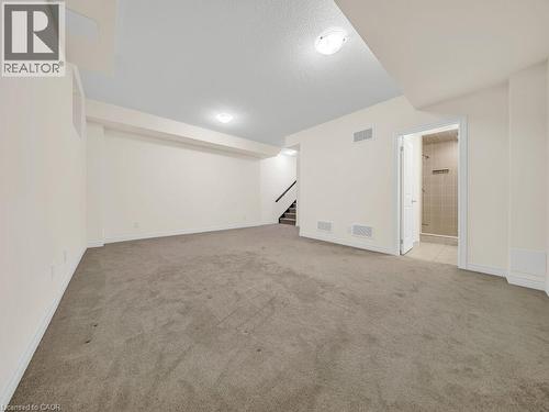 Expansive carpeted room featuring recessed lighting, a staircase with dark railings, and a doorway leading to a tiled shower enclosure - 76 Grassbourne Avenue, Kitchener, ON 