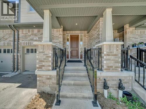 Inviting front porch featuring a brown wood-panel front door, light-colored brick exterior, concrete steps with black metal railings, and a single-car garage with a panel-style door - 76 Grassbourne Avenue, Kitchener, ON 