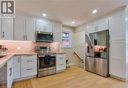 Contemporary kitchen featuring light wood-finish flooring, white shaker-style cabinetry, and stainless steel appliances - 