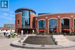 Prominent brick building featuring a cylindrical glass facade, large arched windows, and a paved plaza with tiered stone steps - 