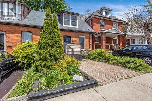 Brick facade residence featuring a front dormer window, dark shingles, and a paved driveway - 30 Sunset Avenue, Hamilton, ON 
