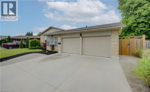 Single-story residence featuring a two-car garage with light-toned doors, stone veneer accents, light-colored siding, and a concrete driveway - 127 Strathcona Crescent, Kitchener, ON 