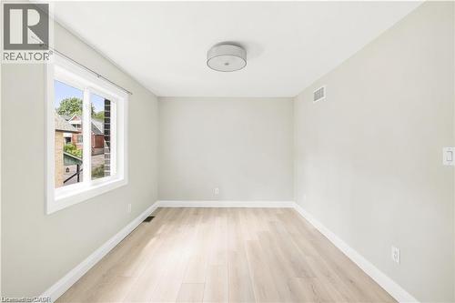 Bright room featuring a large window with white trim, light wood-finish flooring, and a contemporary flush-mount ceiling fixture - 129 St George Street, Kitchener, ON 