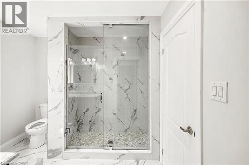 Walk-in shower featuring a glass enclosure, white marble-style wall tiling, and a pebble-stone floor - 129 St George Street, Kitchener, ON 