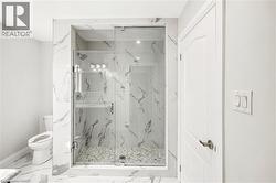 Walk-in shower featuring a glass enclosure, white marble-style wall tiling, and a pebble-stone floor - 
