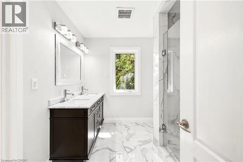Bathroom featuring a double vanity with a dark wood-finish cabinet and light-toned countertop, a shower enclosure with floor-to-ceiling tile, white tile flooring, a single window, and bright overhead - 129 St George Street, Kitchener, ON 