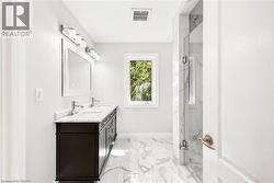 Bathroom featuring a double vanity with a dark wood-finish cabinet and light-toned countertop, a shower enclosure with floor-to-ceiling tile, white tile flooring, a single window, and bright overhead - 