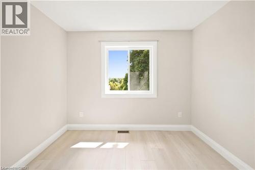 Room featuring a single window, light-toned walls, white baseboards, and wood-finish flooring - 129 St George Street, Kitchener, ON 