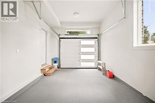 Spacious garage featuring an epoxy-coated concrete floor, modern overhead door with frosted glass panels, and an additional transom window - 129 St George Street, Kitchener, ON 