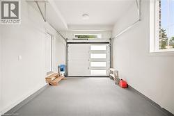 Spacious garage featuring an epoxy-coated concrete floor, modern overhead door with frosted glass panels, and an additional transom window - 