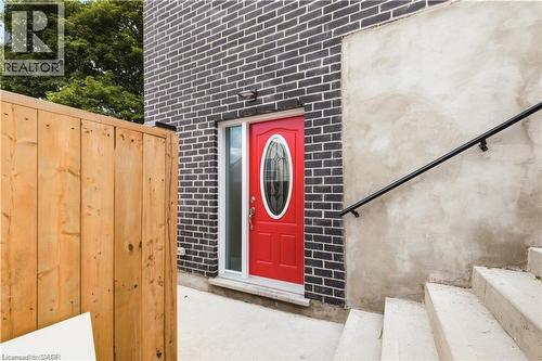 Vibrant red entry door with an oval glass insert, framed by dark brick siding and a natural wood fence - 129 St George Street, Kitchener, ON 