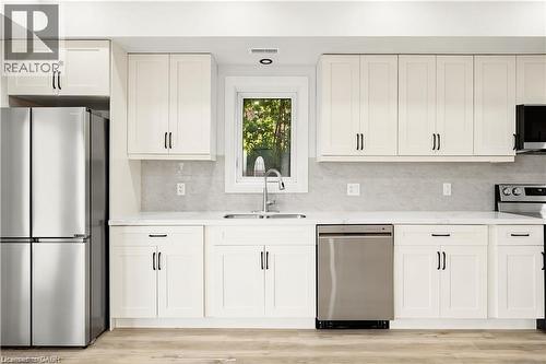 Contemporary kitchen featuring white shaker cabinetry, stainless steel appliances, a light-toned backsplash, and wood-finish flooring - 129 St George Street, Kitchener, ON 