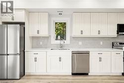 Contemporary kitchen featuring white shaker cabinetry, stainless steel appliances, a light-toned backsplash, and wood-finish flooring - 