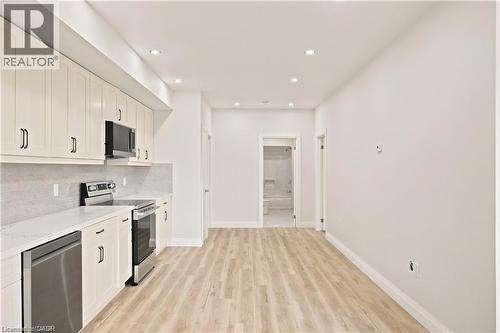 Kitchen featuring light wood-finish flooring, white cabinetry with black hardware, stainless steel appliances, and recessed lighting - 129 St George Street, Kitchener, ON 