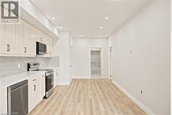 Kitchen featuring light wood-finish flooring, white cabinetry with black hardware, stainless steel appliances, and recessed lighting - 