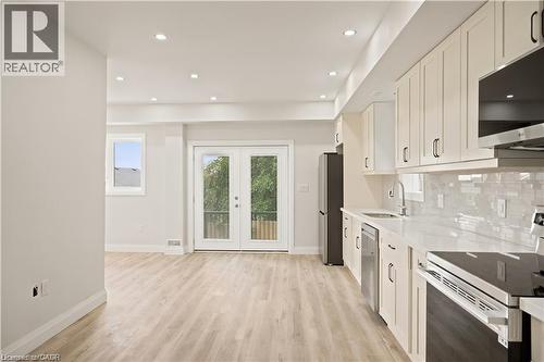 Open concept kitchen featuring light wood-finish flooring, white cabinetry with dark hardware, a white countertop, and a tiled backsplash - 129 St George Street, Kitchener, ON 