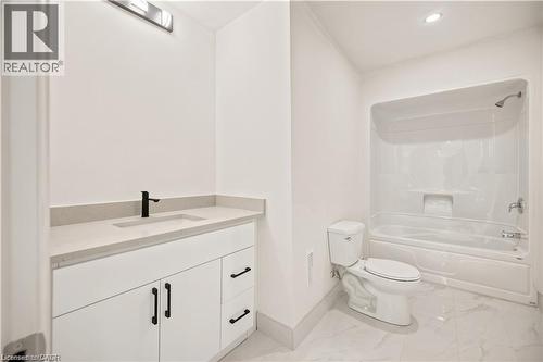 Bathroom featuring white cabinetry with matte black hardware, a light-toned countertop with integrated sink, a matte black faucet, and a combination tub/shower unit - 129 St George Street, Kitchener, ON 