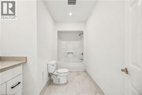 Bathroom featuring a full tub and shower combination, white toilet, and marble-look floor tiling - 129 St George Street, Kitchener, ON 