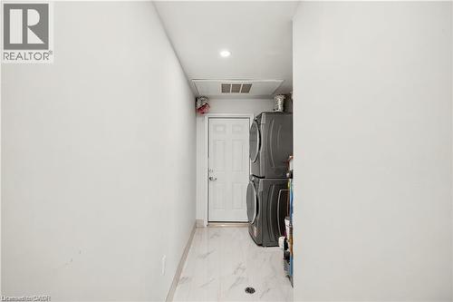Dedicated laundry area featuring stacked appliances, a white panel door, light-toned flooring, and recessed lighting - 129 St George Street, Kitchener, ON 
