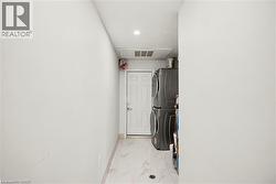 Dedicated laundry area featuring stacked appliances, a white panel door, light-toned flooring, and recessed lighting - 