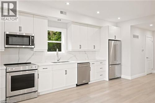 Bright kitchen featuring white cabinetry, stainless steel appliances, a single basin sink, and wood-finish flooring - 129 St George Street, Kitchener, ON 
