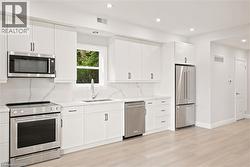 Bright kitchen featuring white cabinetry, stainless steel appliances, a single basin sink, and wood-finish flooring - 