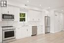 Bright kitchen featuring white cabinetry, stainless steel appliances, a single basin sink, and wood-finish flooring - 129 St George Street, Kitchener, ON 