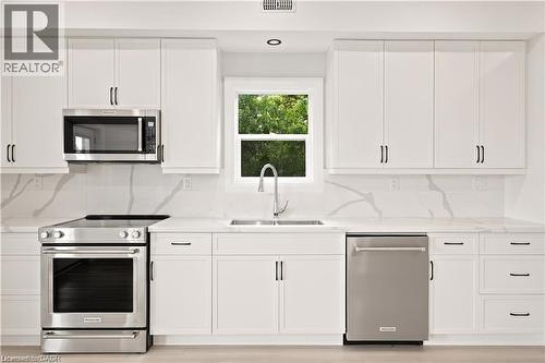 Contemporary kitchen featuring white shaker cabinetry, stainless steel appliances, a white farmhouse sink, and stone countertops with a matching backsplash - 129 St George Street, Kitchener, ON 
