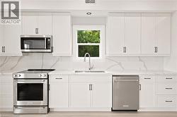 Contemporary kitchen featuring white shaker cabinetry, stainless steel appliances, a white farmhouse sink, and stone countertops with a matching backsplash - 