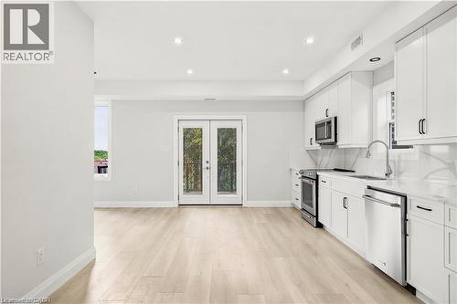 Open-concept kitchen featuring white cabinetry, stainless steel appliances, and light wood-finish flooring - 129 St George Street, Kitchener, ON 