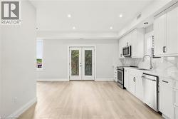 Open-concept kitchen featuring white cabinetry, stainless steel appliances, and light wood-finish flooring - 