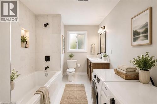 Bathroom featuring a built-in tub with matte black fixtures and a tiled surround, a window providing natural light, a vanity with wood-finish cabinetry and a single-basin sink, and a stacked washer an - 129 St George Street, Kitchener, ON 