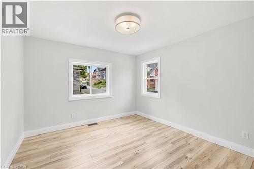 Spacious interior room featuring light wood-finish flooring, white baseboards, and two distinct windows - 131 St George Street, Kitchener, ON 