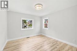 Spacious interior room featuring light wood-finish flooring, white baseboards, and two distinct windows - 