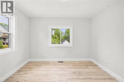 Bright interior space featuring light wood-finish flooring, white baseboards, and two windows with white trim - 