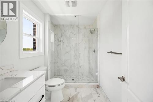 Full bathroom featuring a glass-enclosed shower with a tiled interior, a vanity with an integrated sink, and white marble-look flooring - 131 St George Street, Kitchener, ON 