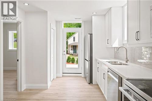 Modern kitchen featuring white cabinetry, light-toned wood-finish flooring, stainless steel appliances, a double basin sink with a gooseneck faucet, and light-colored countertops - 131 St George Street, Kitchener, ON 