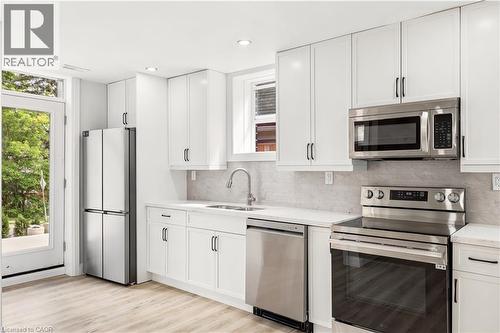 Modern kitchen featuring white shaker cabinetry, stainless steel appliances, light wood-finish flooring, a white countertop, and a textured backsplash - 131 St George Street, Kitchener, ON 