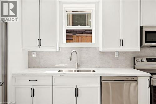 Bright kitchen featuring white shaker cabinetry, stainless steel appliances, a double basin sink with a gooseneck faucet, and a light-toned backsplash - 131 St George Street, Kitchener, ON 