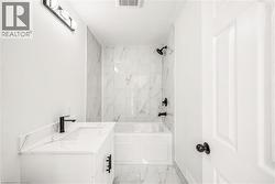 Bathroom featuring a white vanity with an integrated sink and quartz-finish countertop, matte black faucet, and a wall-mounted light fixture - 
