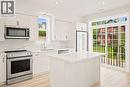 Modern kitchen featuring white cabinetry, stainless steel appliances, a center island with a stone countertop, wood-finish flooring, and a sliding glass door leading to a balcony - 131 St George Street, Kitchener, ON 