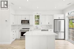 Modern kitchen with a central island, white cabinetry, integrated stainless steel appliances, marble-patterned countertops and backsplash, and wood-finish flooring - 