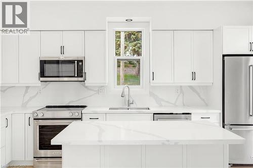 Modern kitchen featuring white cabinetry, stainless steel appliances, a center island with a stone-finish countertop, and a coordinating stone-finish backsplash - 131 St George Street, Kitchener, ON 