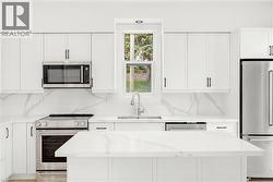 Modern kitchen featuring white cabinetry, stainless steel appliances, a center island with a stone-finish countertop, and a coordinating stone-finish backsplash - 