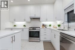 Modern kitchen featuring white cabinetry, stainless steel appliances, a tile backsplash, and light-toned countertops - 