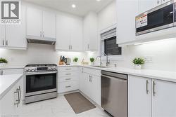 Contemporary kitchen with white cabinetry, stainless steel appliances, white subway tile backsplash, white countertops, and recessed lighting - 